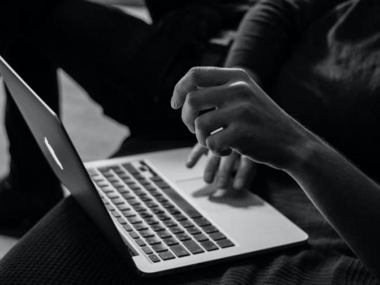 black and white image of laptop showing hands using the keypad